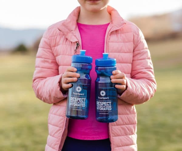 Young girl holding two blue TrueSport branded water bottles.