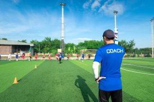 man wearing shirt that says coach on sidelines of a youth soccer game