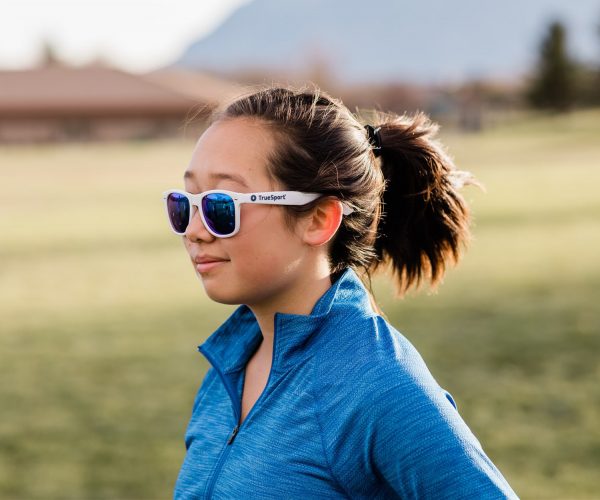 A young woman wearing TrueSport branded blue mirror lens sunglasses.